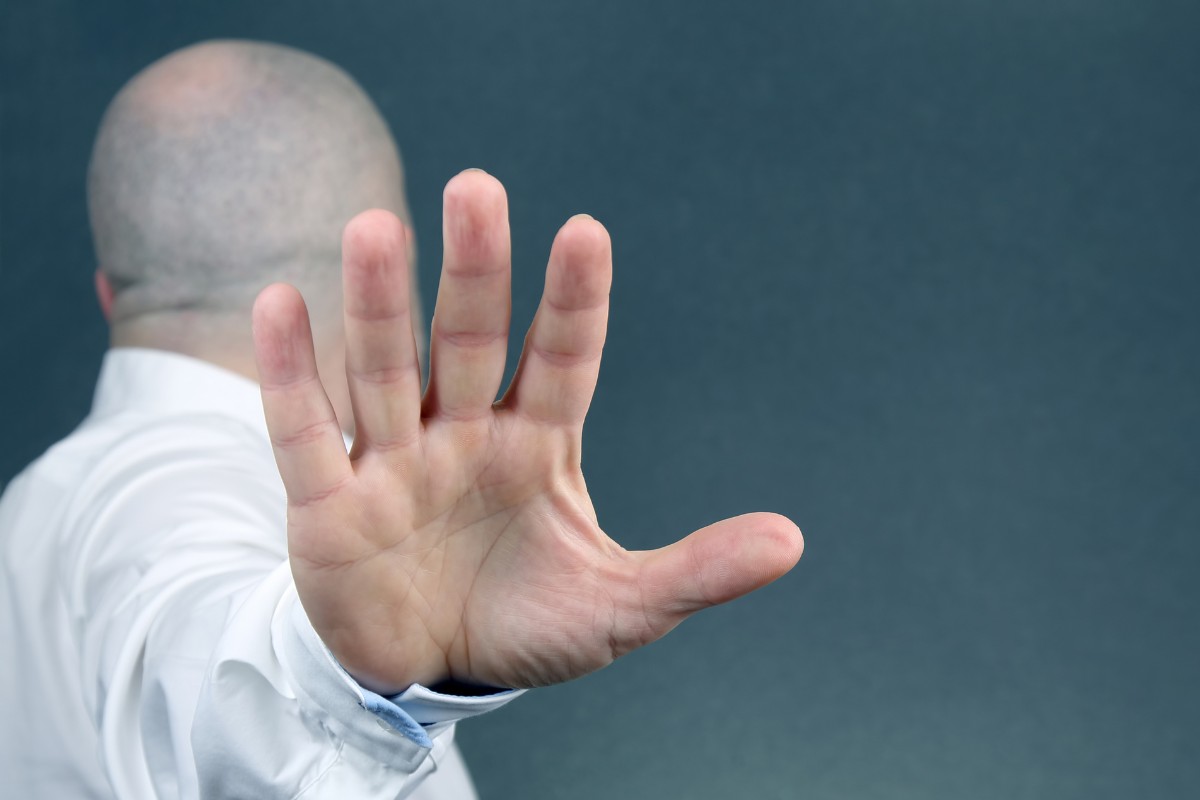 A person, seen from the back, extends their hand with the palm facing outward in a "stop" gesture.