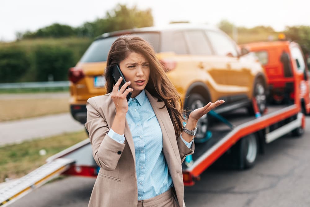woman calling someone while towing service helping her on the road